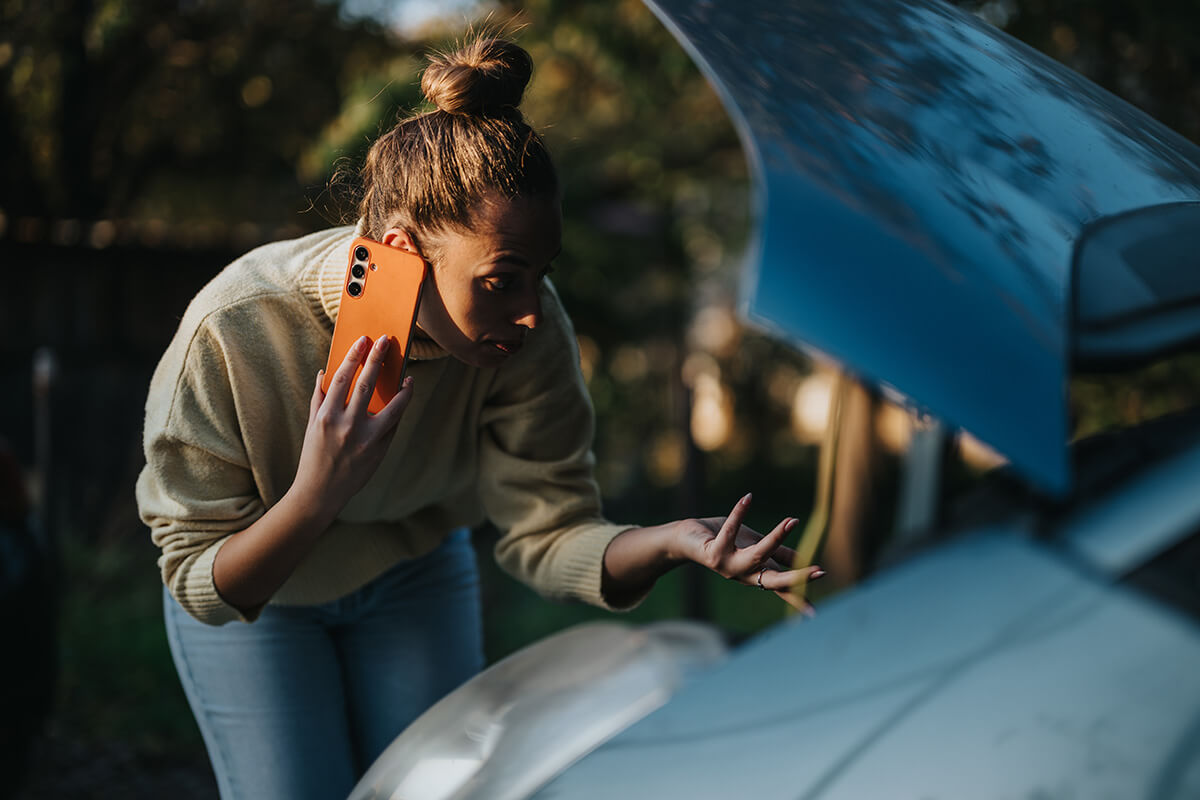 A concerned woman stands beside her car with the hood open A concerned woman stands beside her car with the hood open
